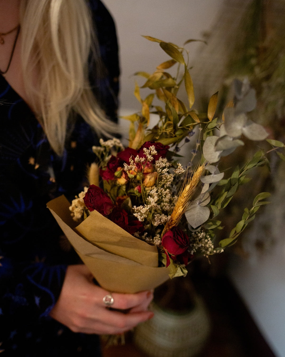 Person holding a bouquet of dried flowers with dried florals hanging from the ceiling.