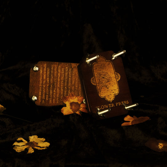 Handmade wooden flower press, with engraved floral design and poem in the wood. Pressed flowers surround the frames on velvet fabric background