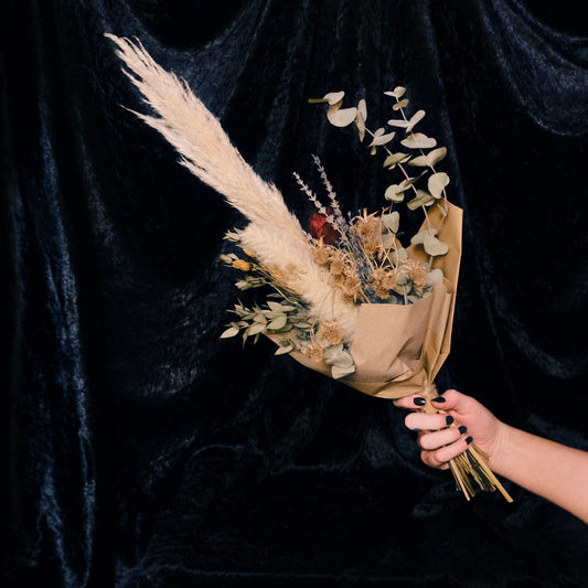 Bouquet of dried flowers held by a hand against a dark background