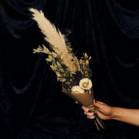 Hand holding a bouquet of dried flowers and pampas grass against a dark background