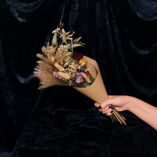 Hand holding a bouquet of dried flowers against a dark background