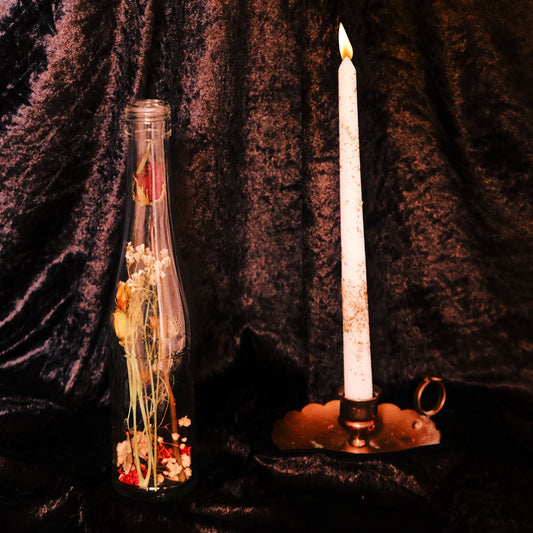 Decorative bottle with flowers and a lit candle on a dark background