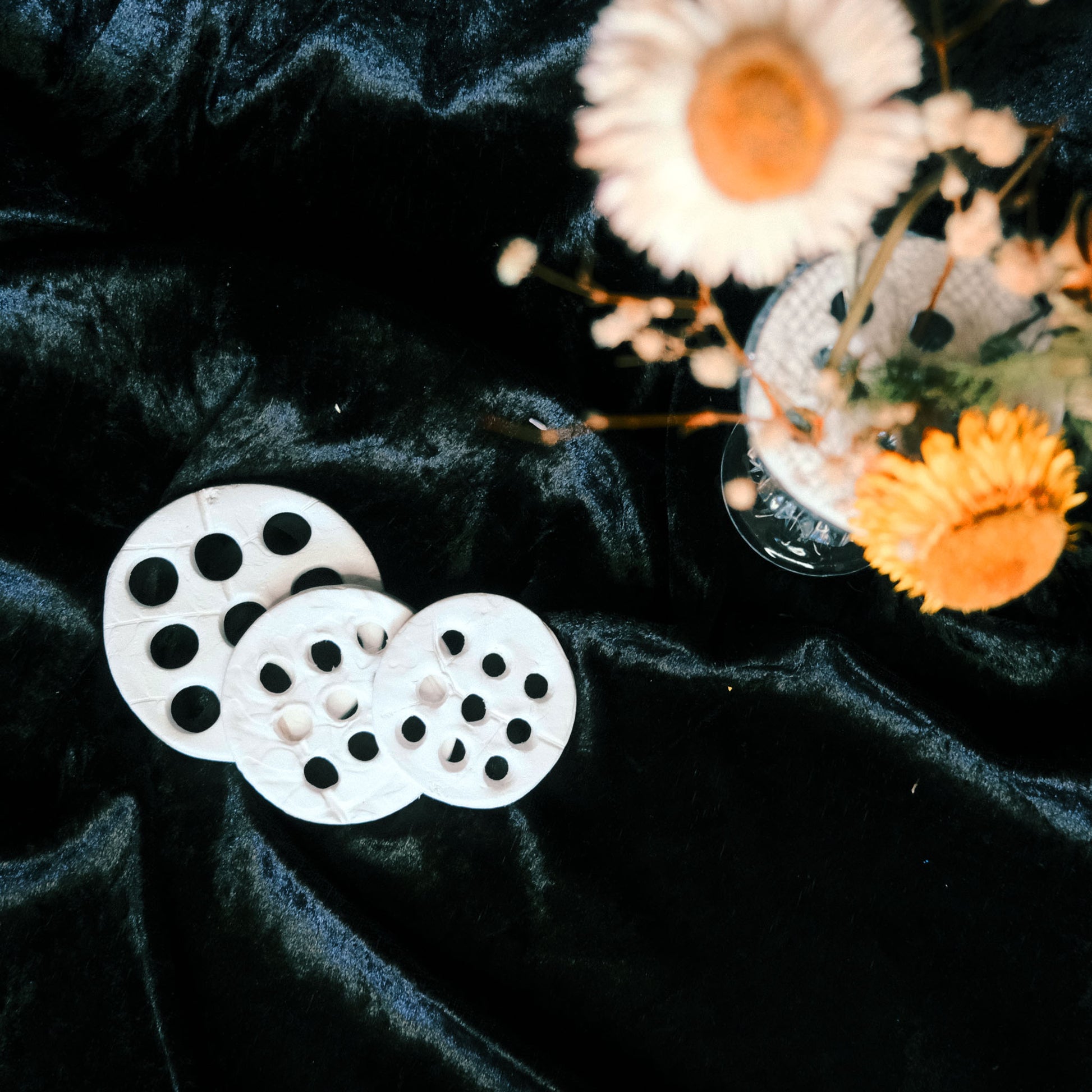 White circular clay flower frog for sustainable flower arranging, placed on dark velvet fabric background with dried flowers.