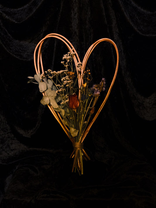 Heart-shaped arrangement of dried flowers in a copper wire frame on a black background