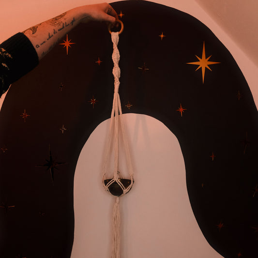 Person holding a macrame plant hanger against a dark background with star decorations