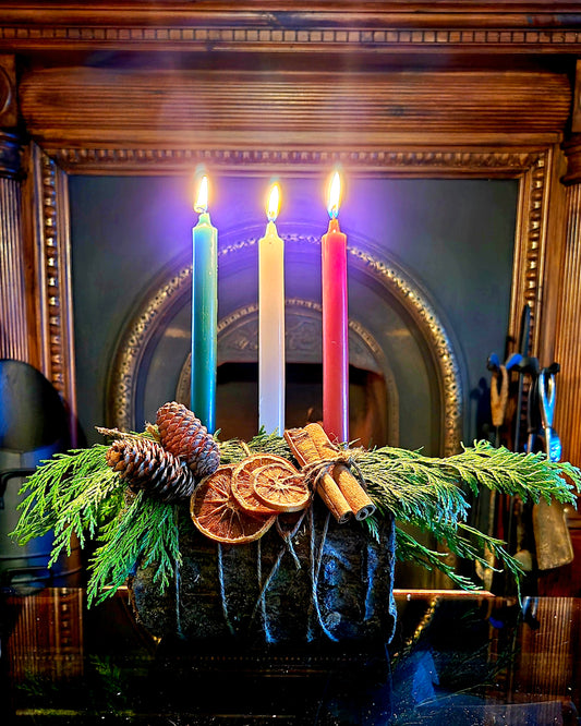 Decorative yule log arrangement with candles, pine cones, and cinnamon sticks in front of a mirror.